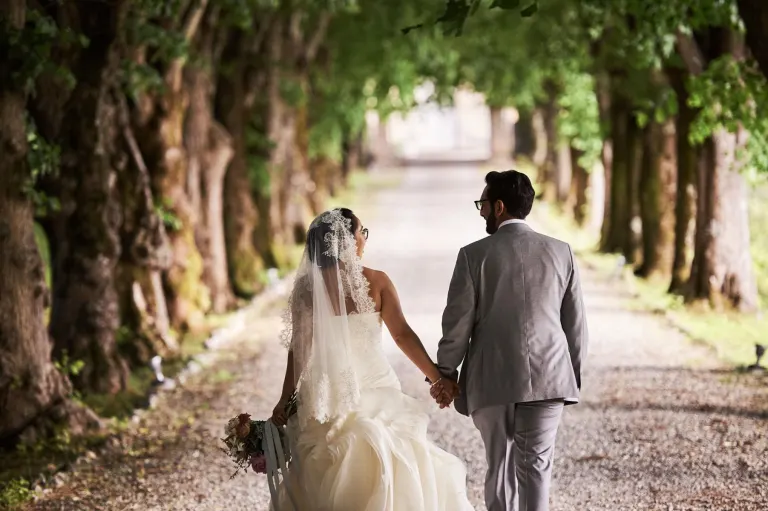 Bride and groom walking under an avenue of trees