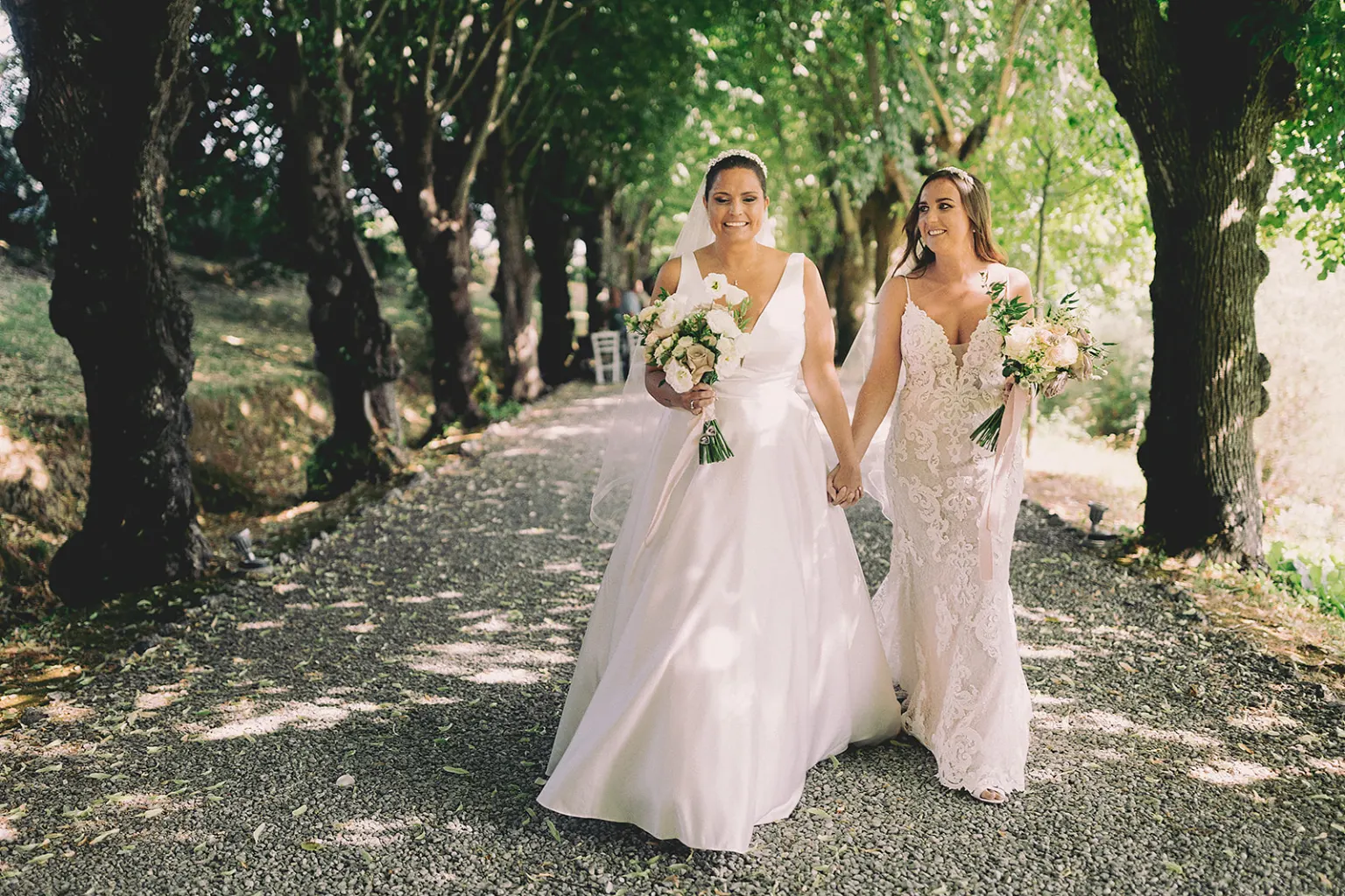 A civil union Two brides with their bouquets on a tree-lined avenue