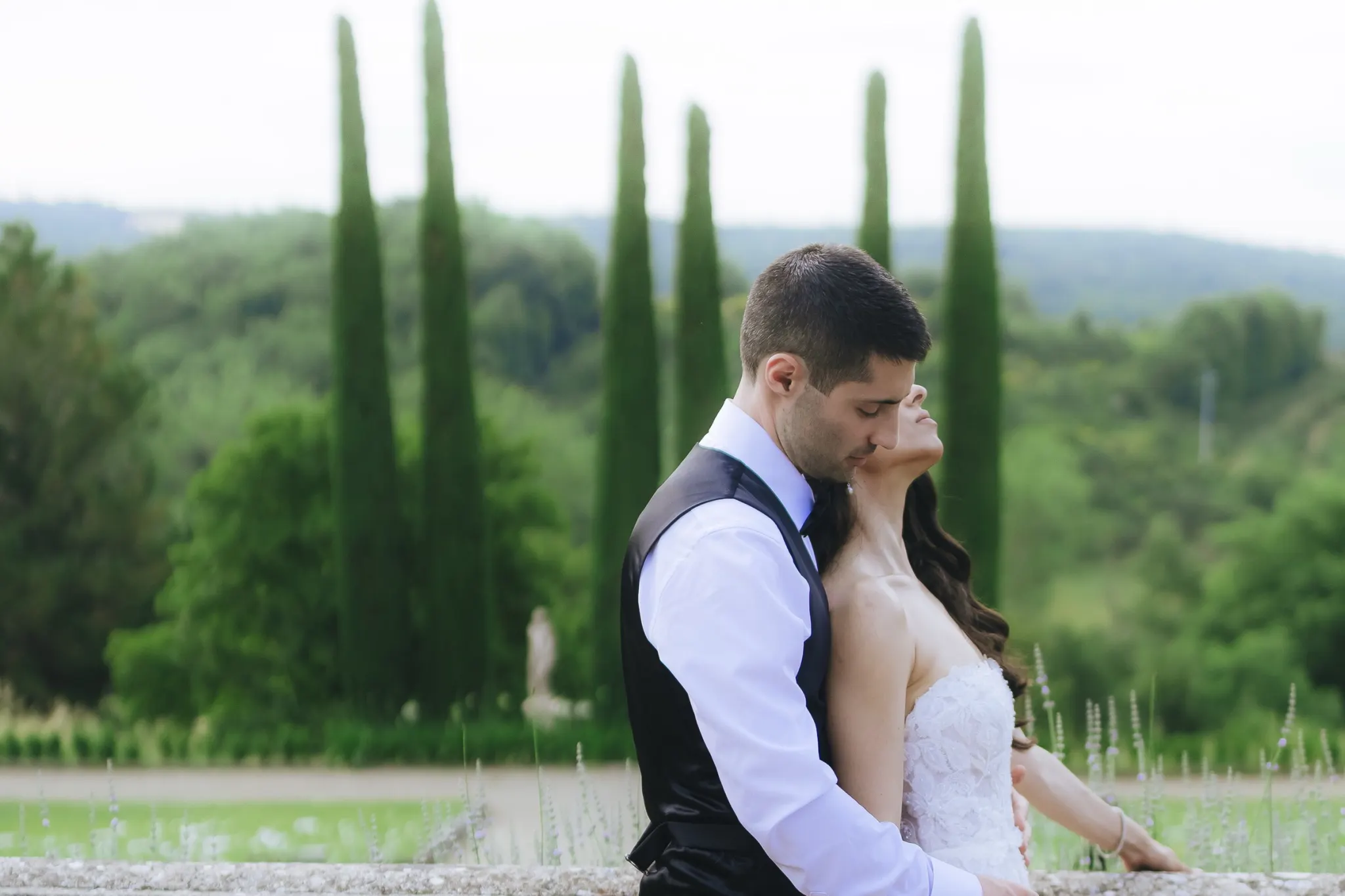 Efffetti® Wedding Planners In Tuscany - Italy Bride and groom embracing on a stone balustrade above the Tuscan hills and cypresses