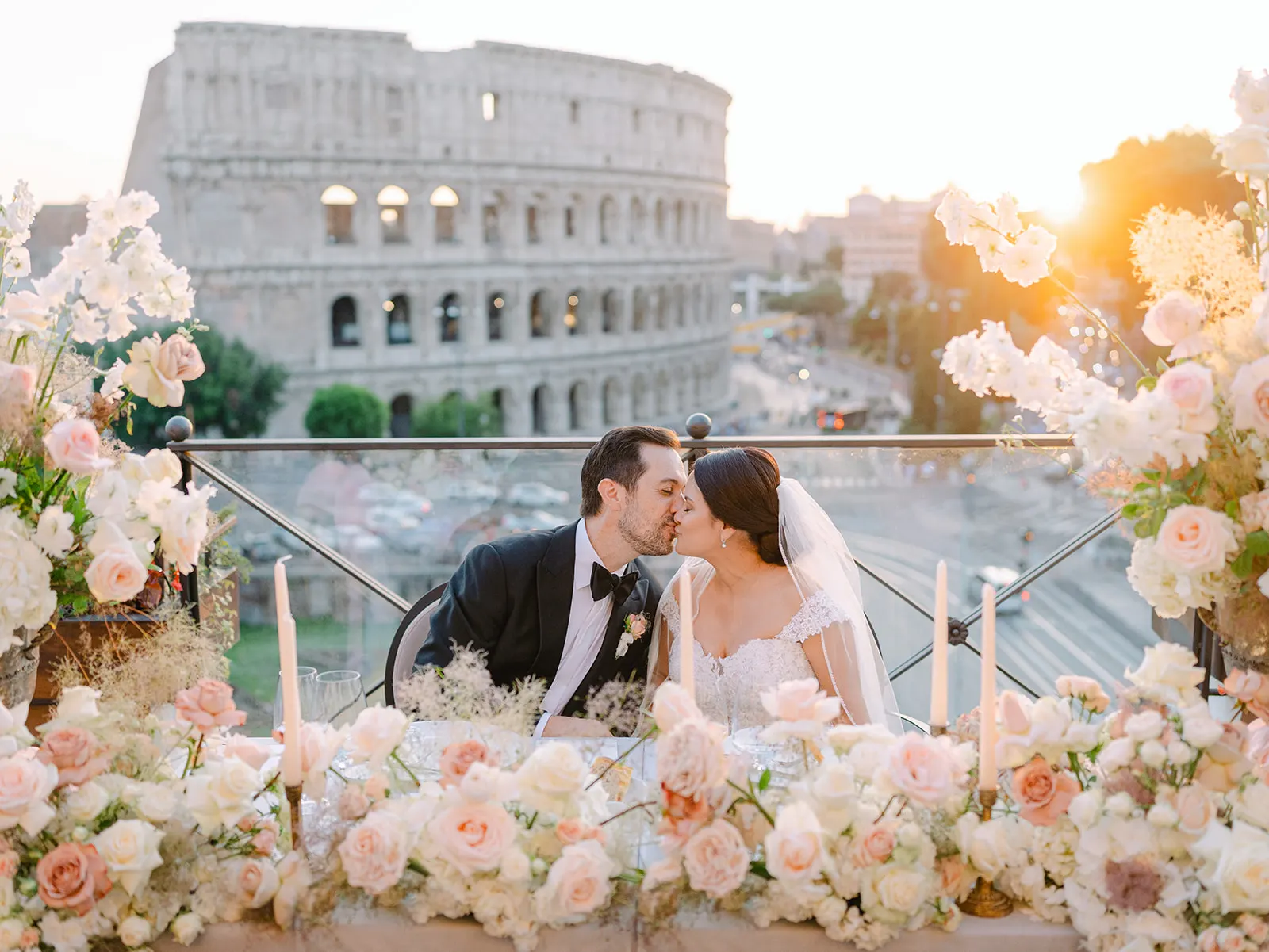 Efffetti® Wedding Planners In Tuscany - Italy Bride and groom kissing at a flower-covered table on a terrace overlooking the Colosseum in Rome
